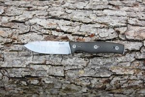 A fixed-blade knife with a textured dark handle and a shiny, slightly weathered blade is resting horizontally on rough tree bark.