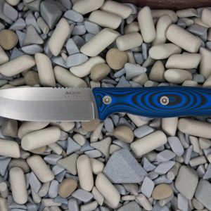 A fixed-blade knife with a blue and black patterned handle lies on a bed of smooth, assorted gray and white pebbles and stones.