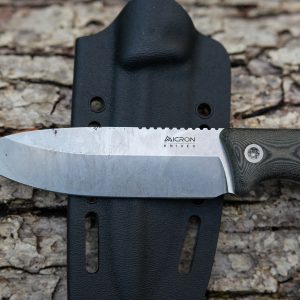 A Micron MK-4 fixed-blade knife with a textured black handle rests on its black sheath, set atop rough tree bark.